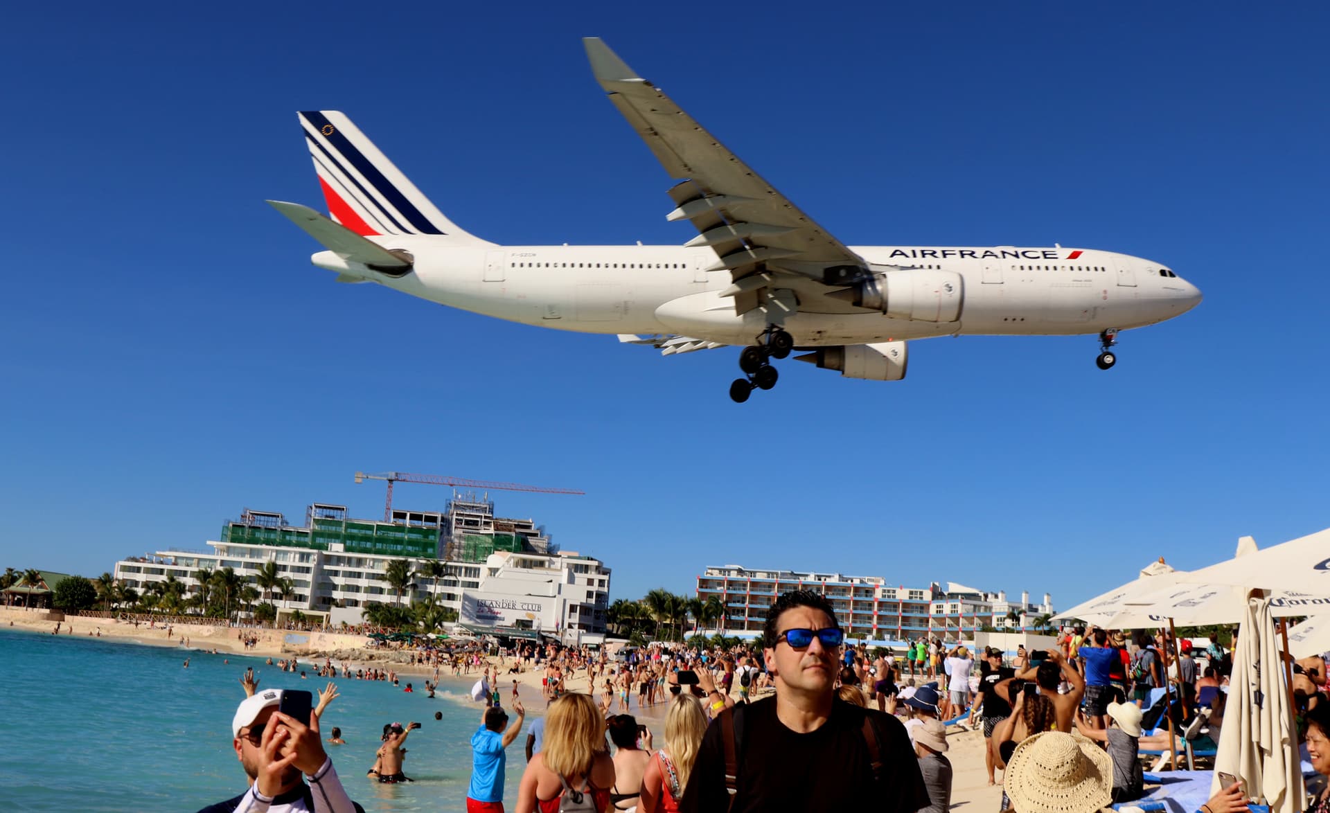 A wide-body jet passing low over swimmers and sunbathers at Maho Beach on its way to land