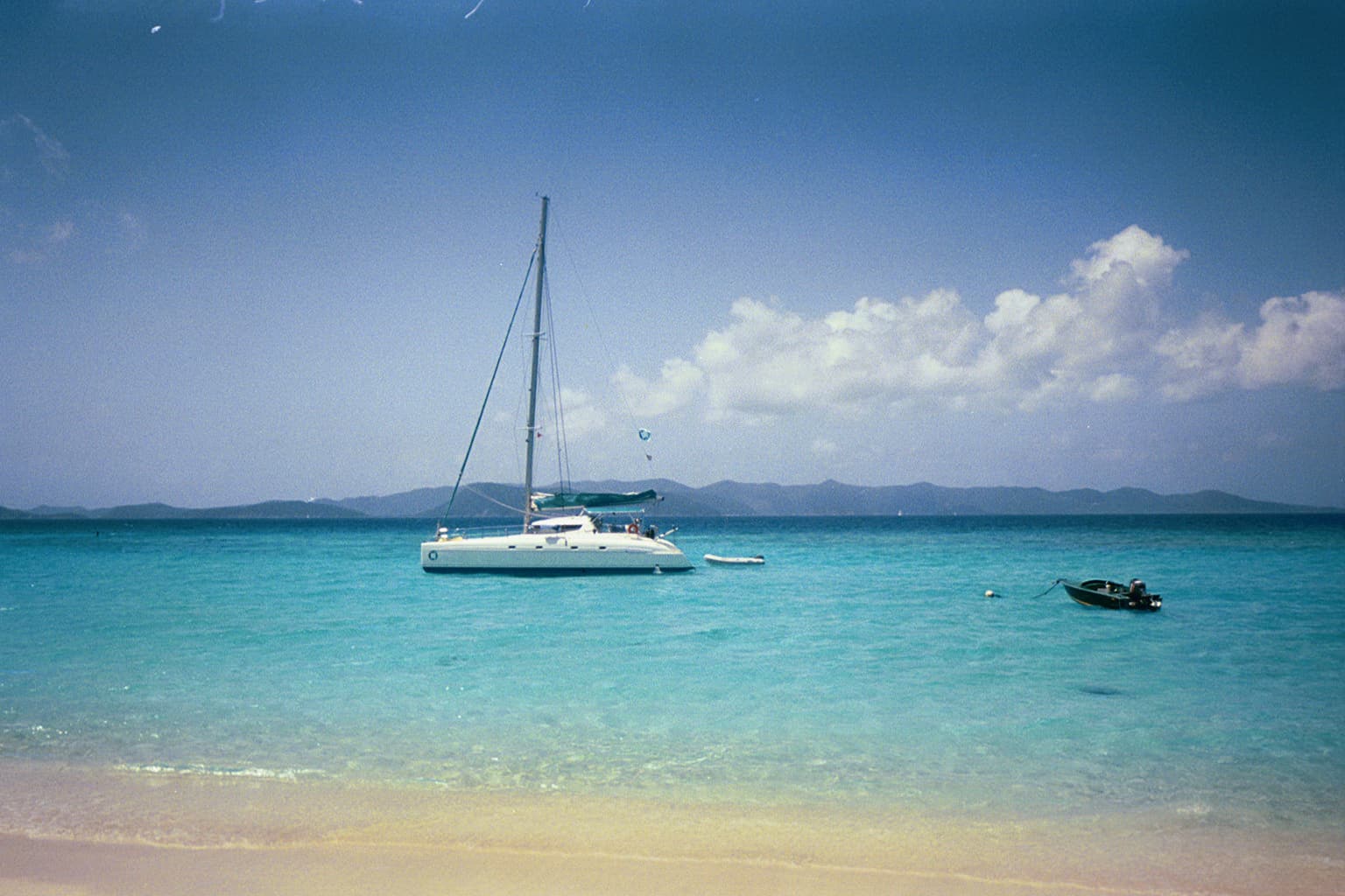 A catamaran anchored off a sandy beach in clear turquoise water